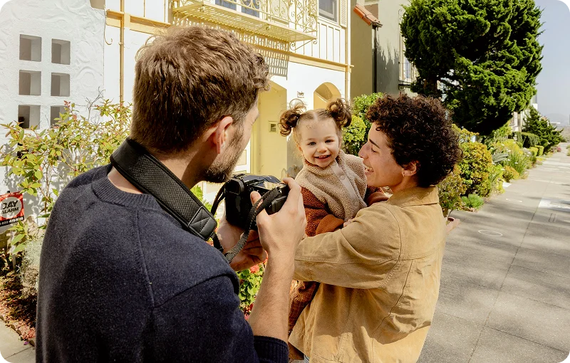 @lang('Família sorridente com uma criança ao colo, fotografada num momento feliz após transferir o crédito habitação e aliviar encargos mensais.')